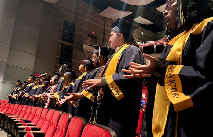  The class of 2025 wearing their cap and gowns and holding out their hands
